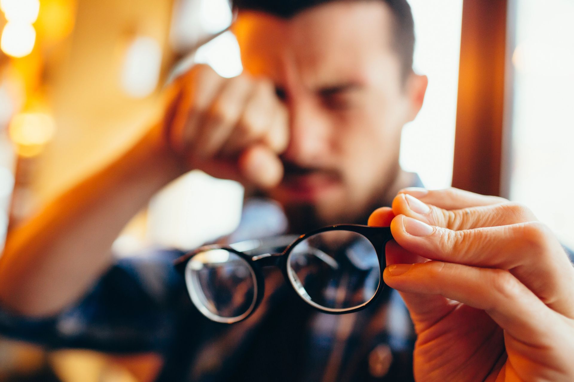 A man is holding a pair of glasses in his hand and rubbing his eyes.