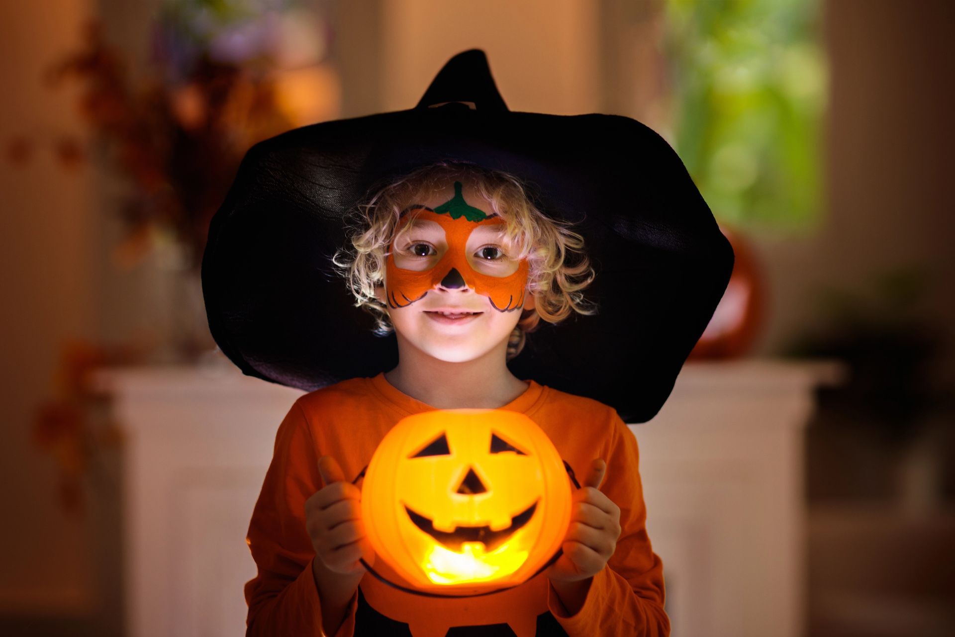 A young boy in a witch costume is holding a pumpkin.