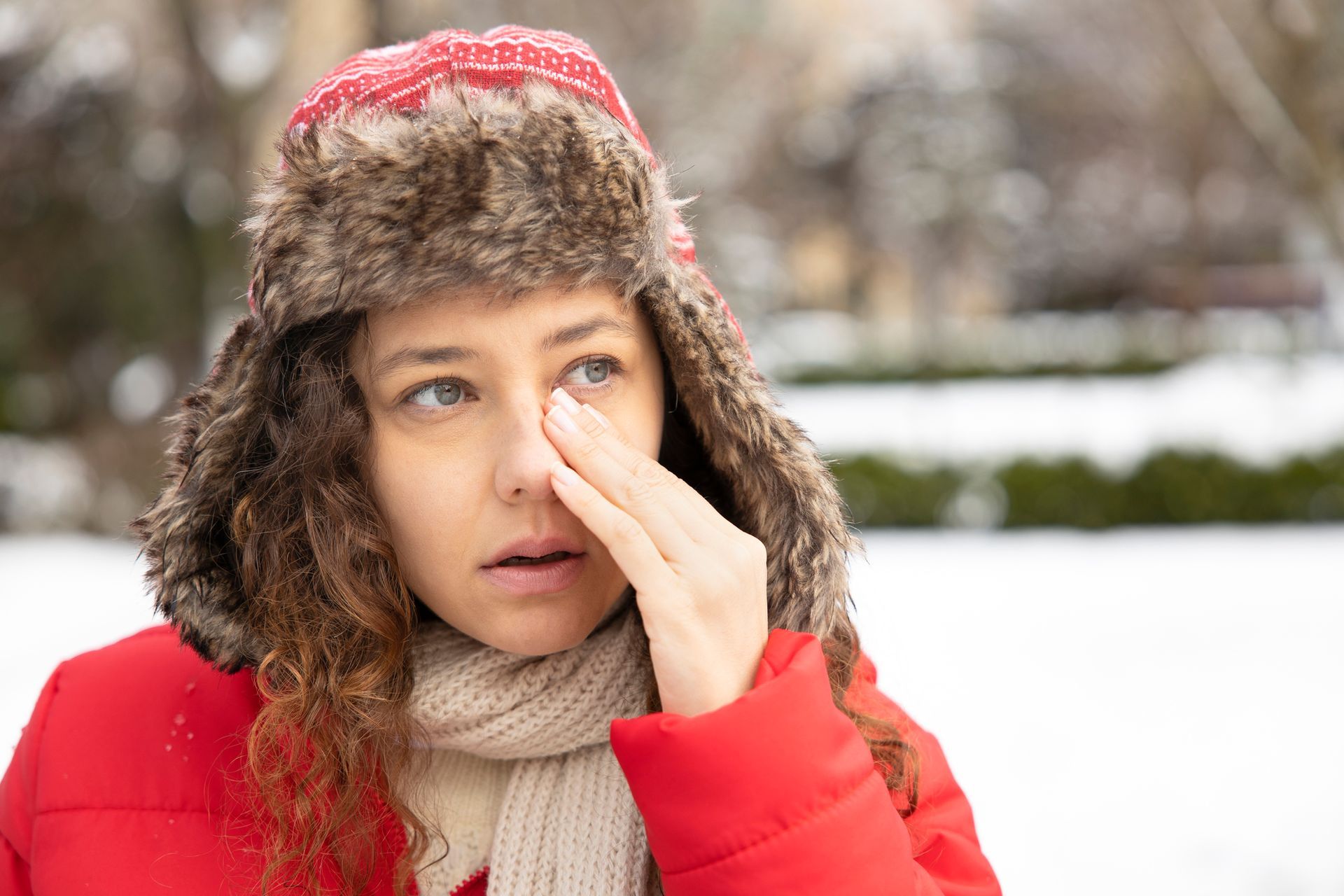 A woman wearing a fur hat and scarf is scratching her eye