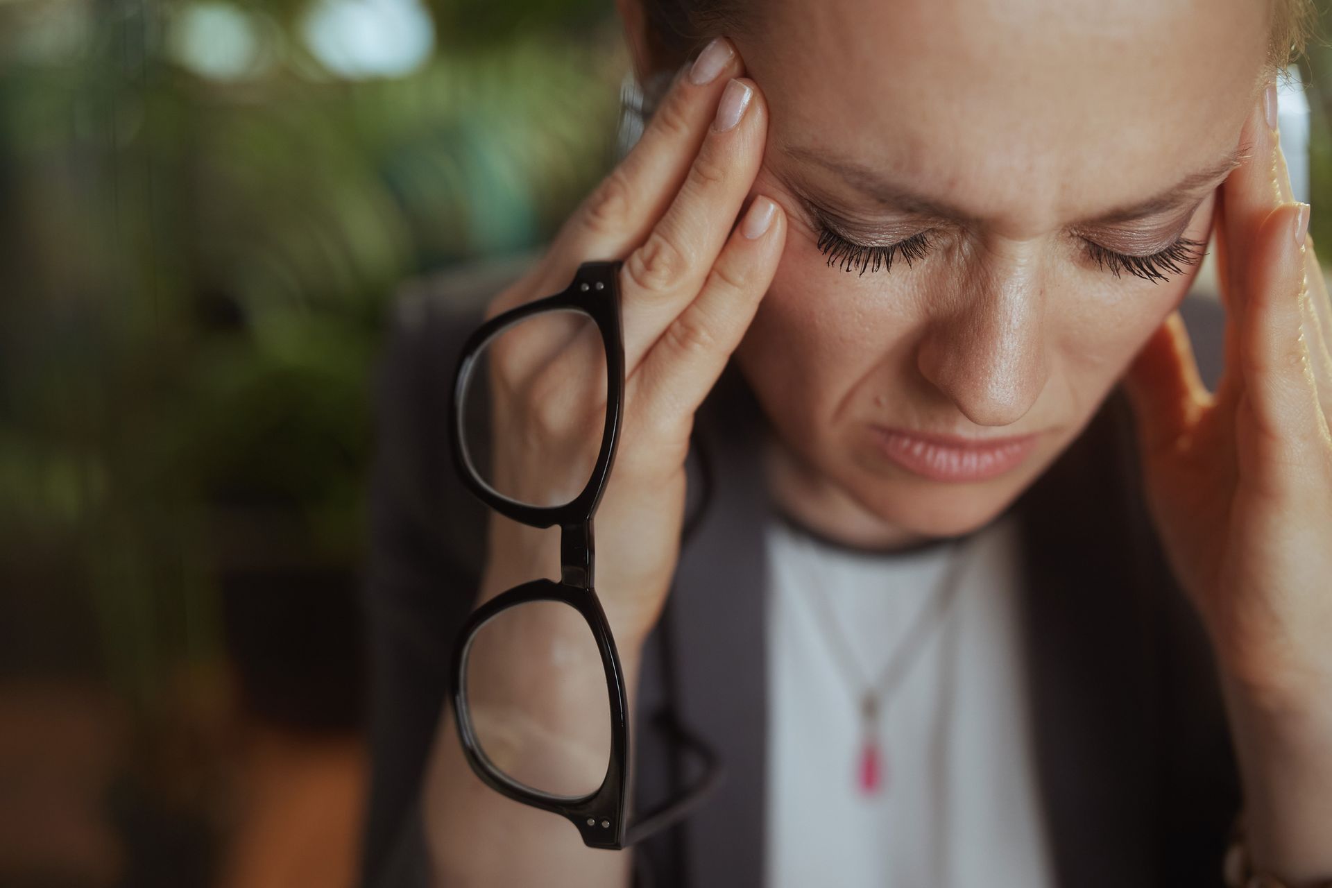 A woman wearing glasses is holding her head in pain.