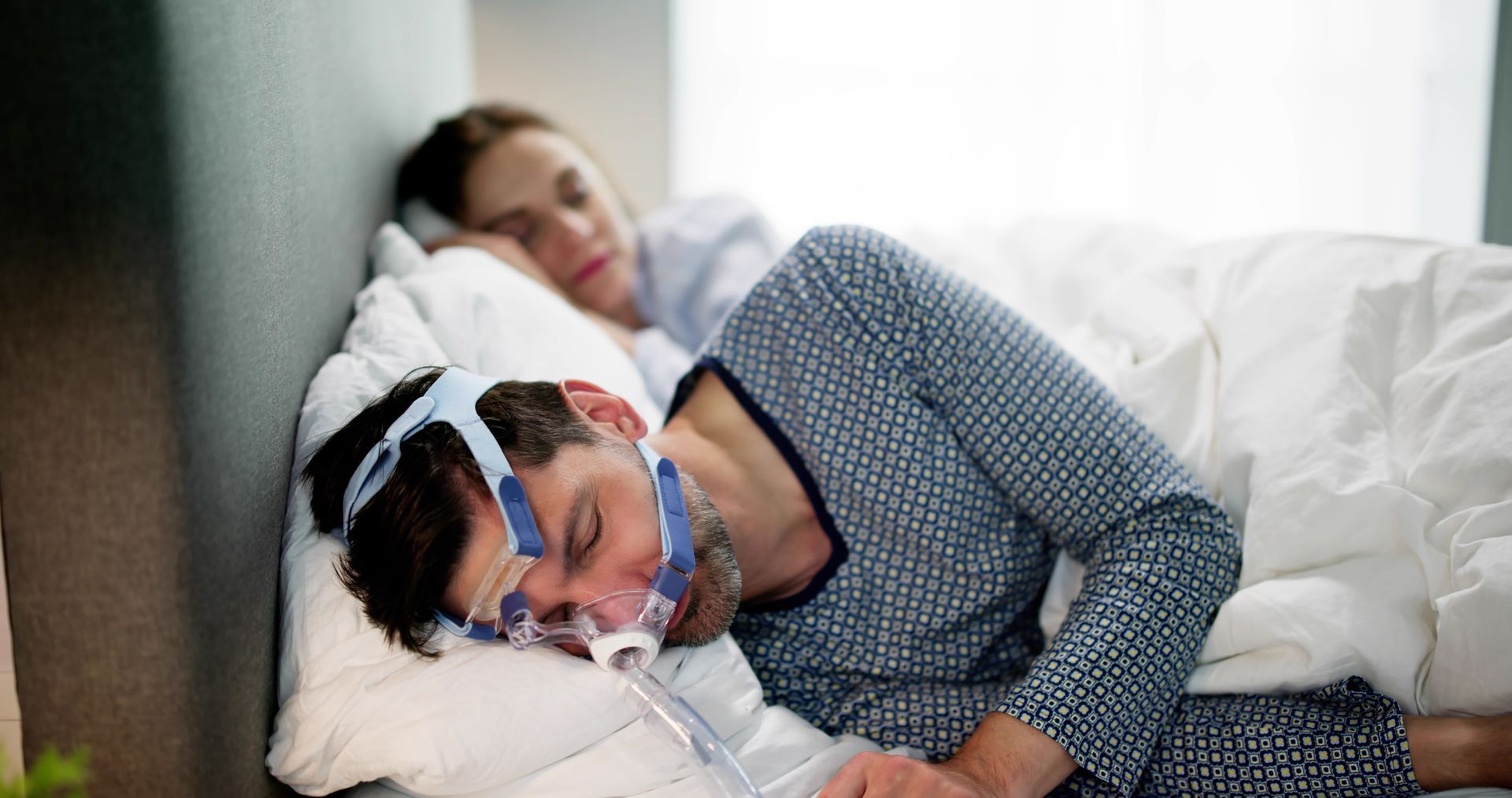 A man is sleeping in a bed with a cpap mask on his face.