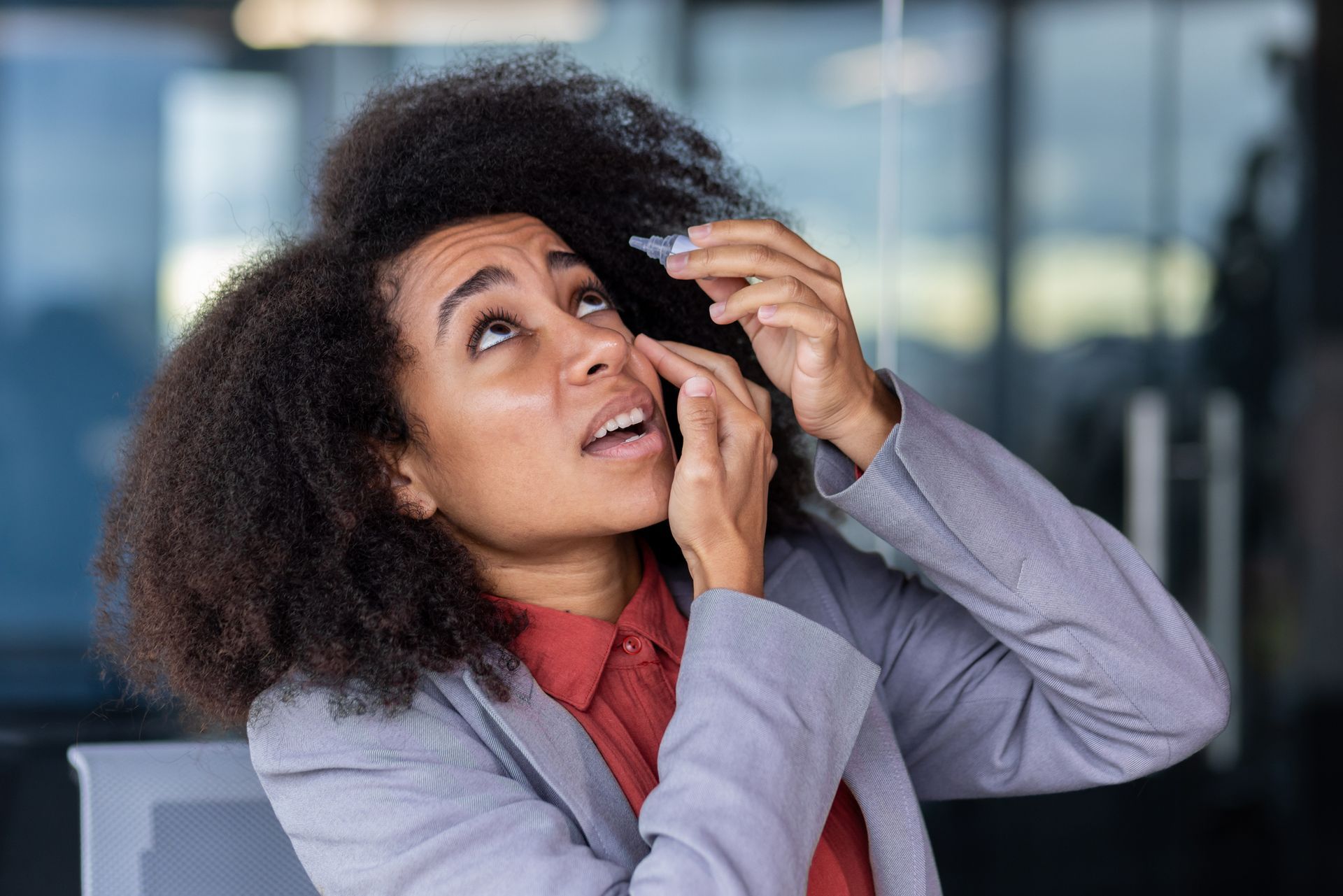 A woman is applying eye drops to her eyes.