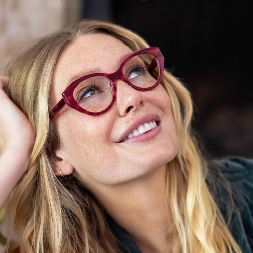 A woman wearing designer glasses is smiling and looking up.