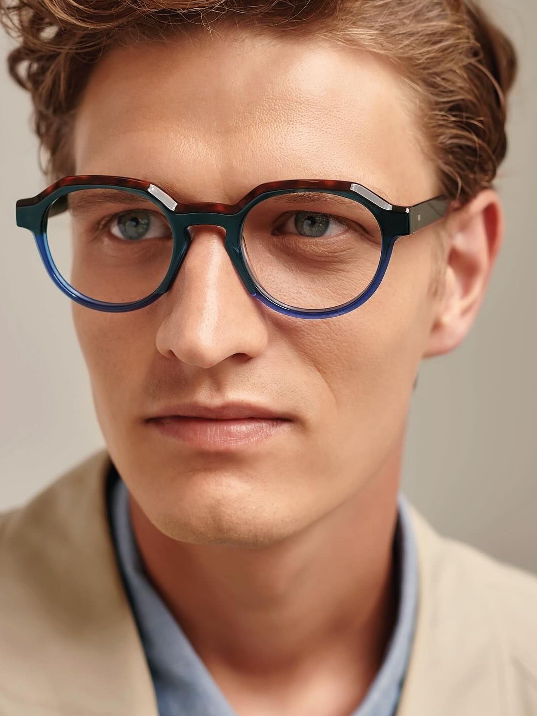 A close up of a man wearing glasses and a tan jacket