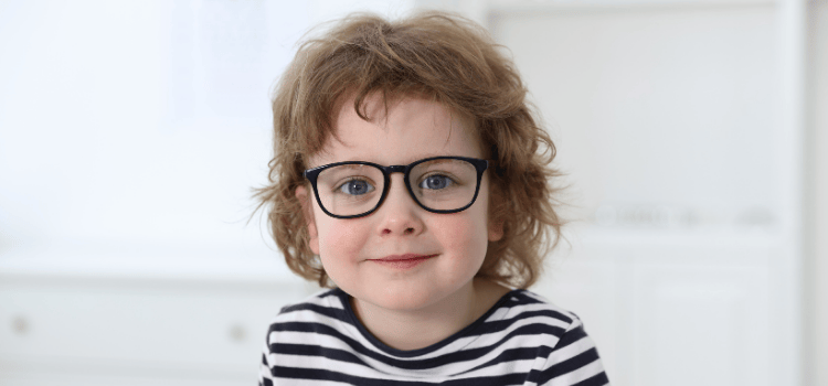 Child with curly hair wearing glasses and striped shirt, smiling at the camera.