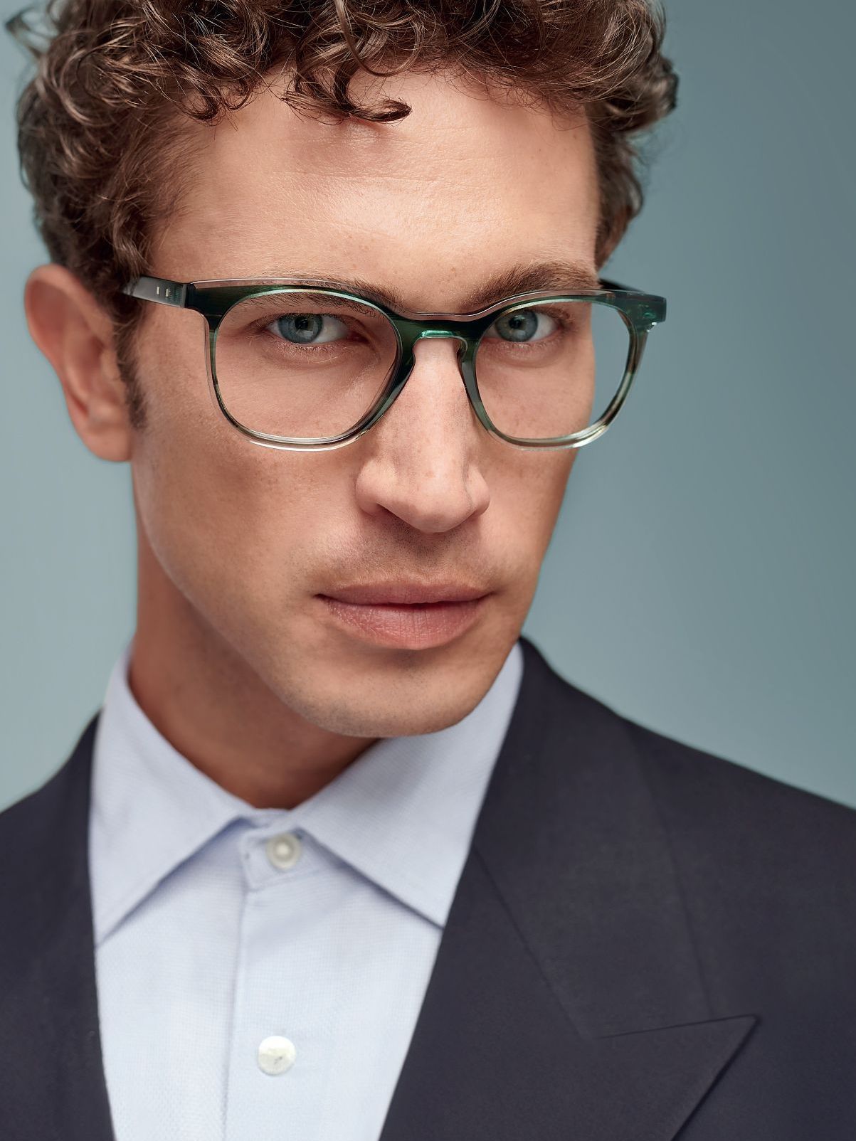 A man with curly hair wearing glasses and a suit