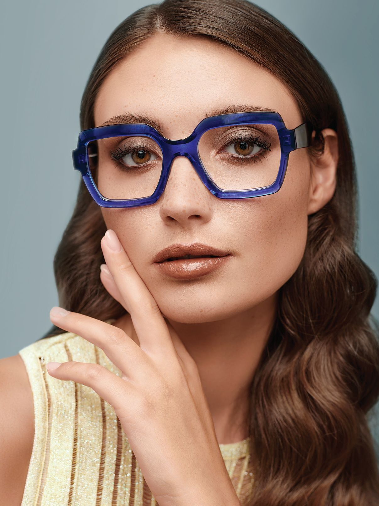 A woman wearing glasses is standing in front of a blue wall.