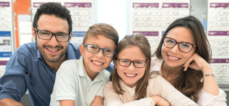 Family smiling and wearing glasses in an optician's store.