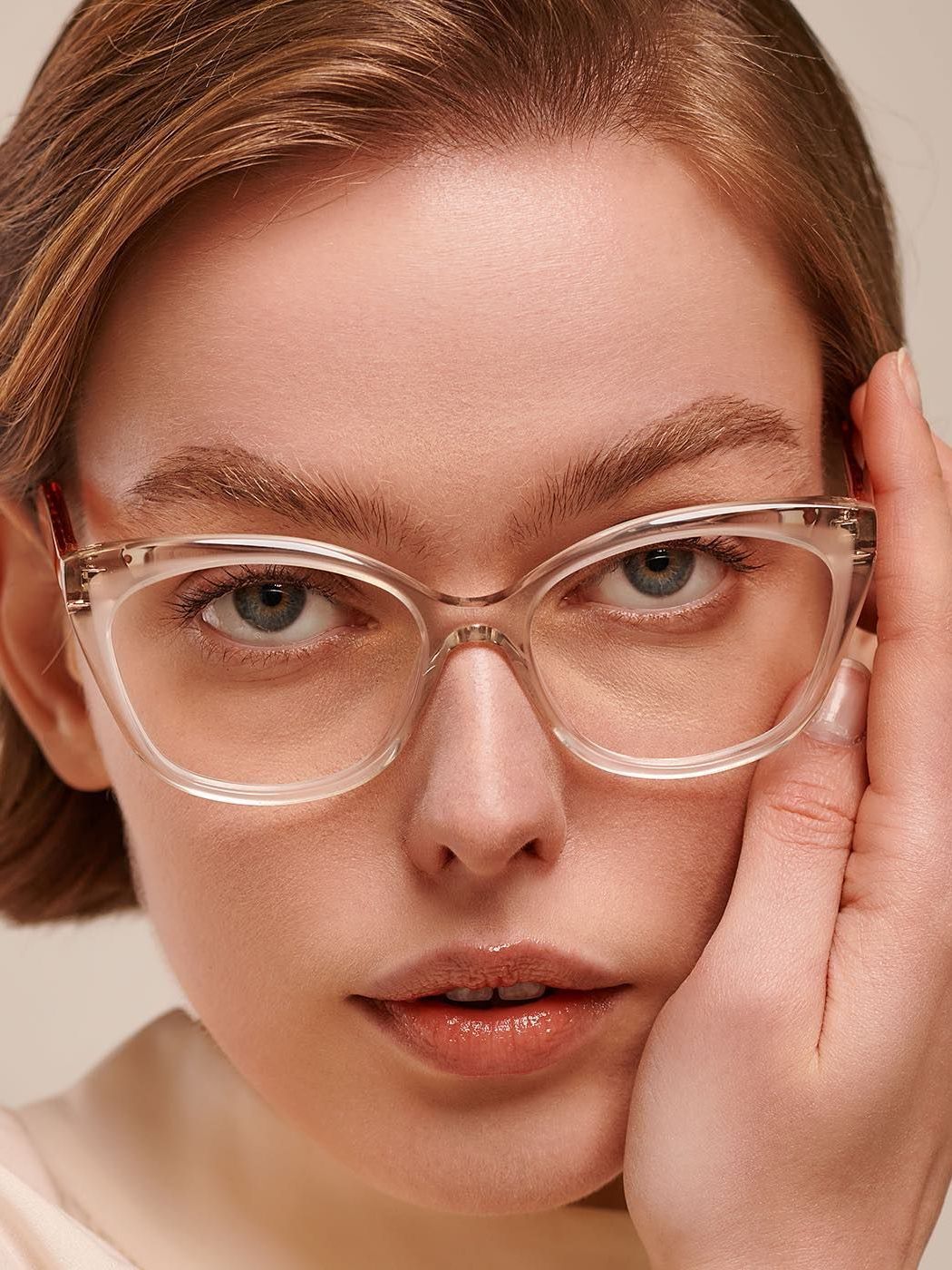 A woman wearing glasses is touching her face with her hand.