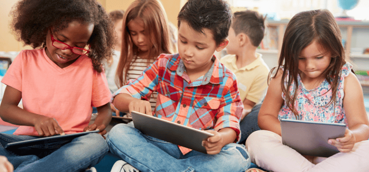 Children sitting cross-legged, using tablets in a classroom.