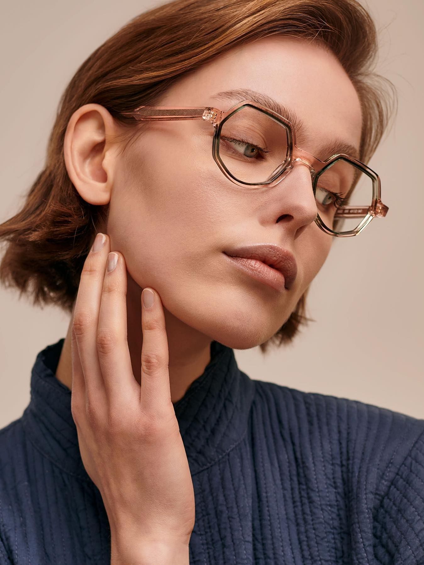 A woman wearing glasses is touching her face.