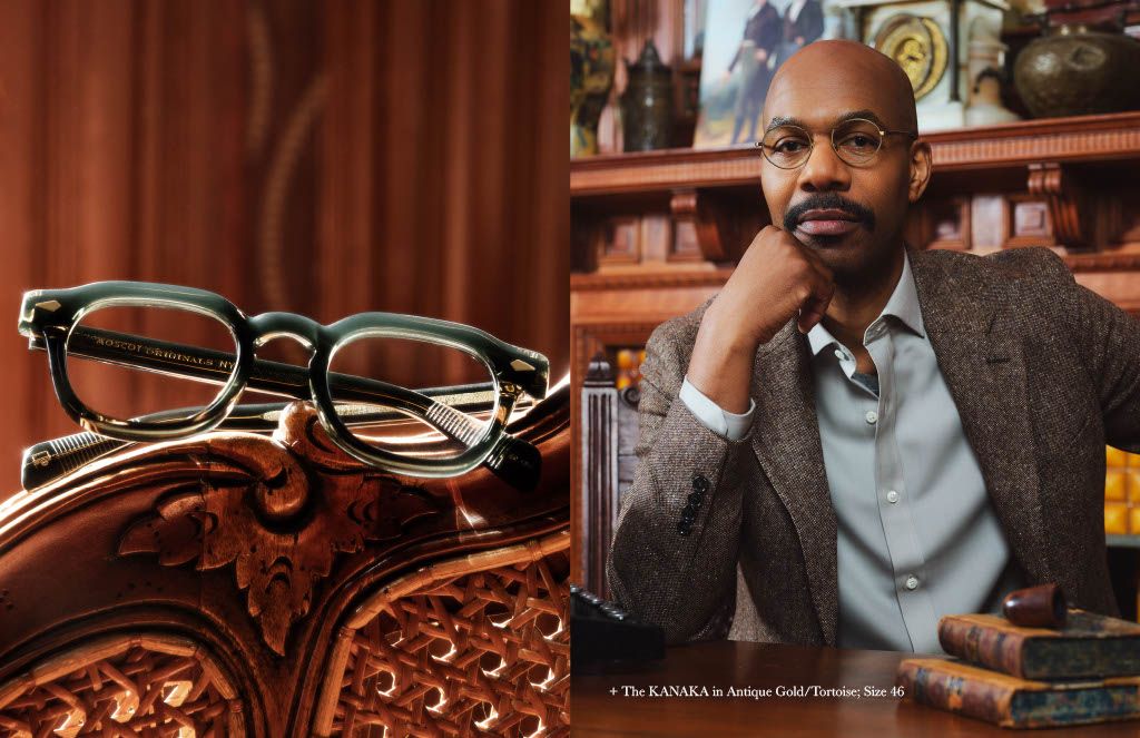 A man wearing glasses is sitting at a table with books.