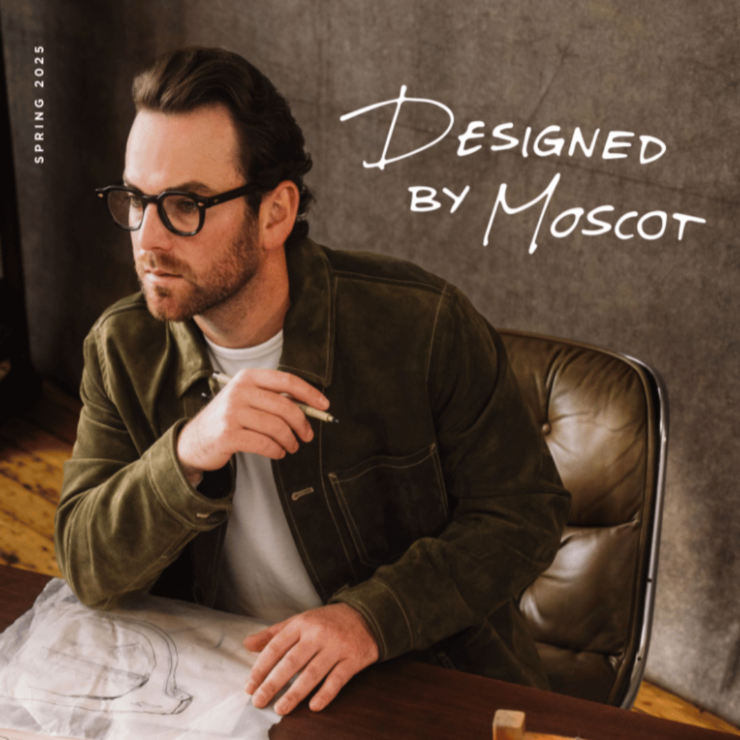 A man wearing glasses is sitting at a desk with a drawing on it.