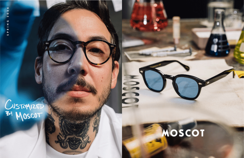 Man wearing black glasses beside MOSCOT eyeglasses on a table with tools in a workshop-style setting