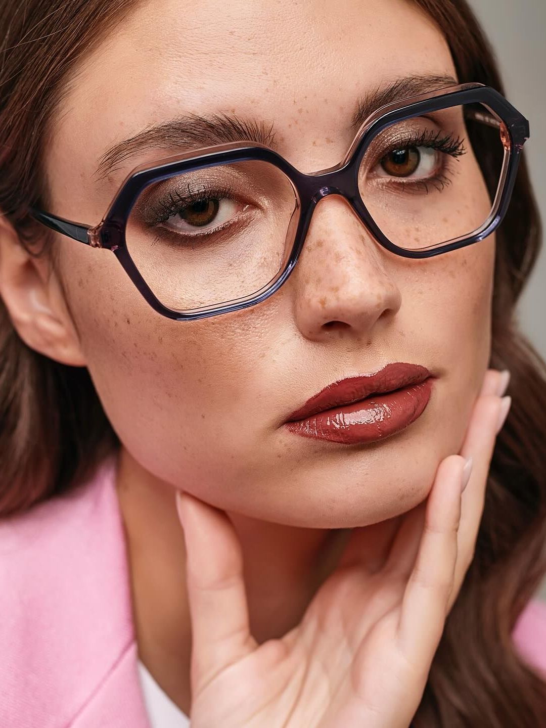 A woman wearing glasses and a pink jacket is touching her face.