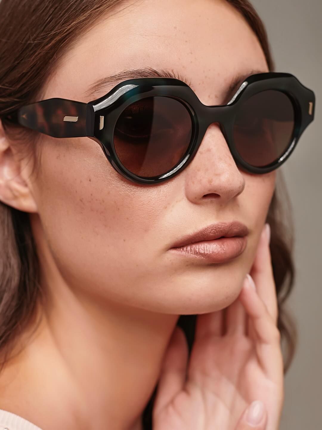 A close up of a woman wearing sunglasses and touching her face