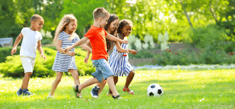 Children playing soccer on a grassy field on a sunny day.