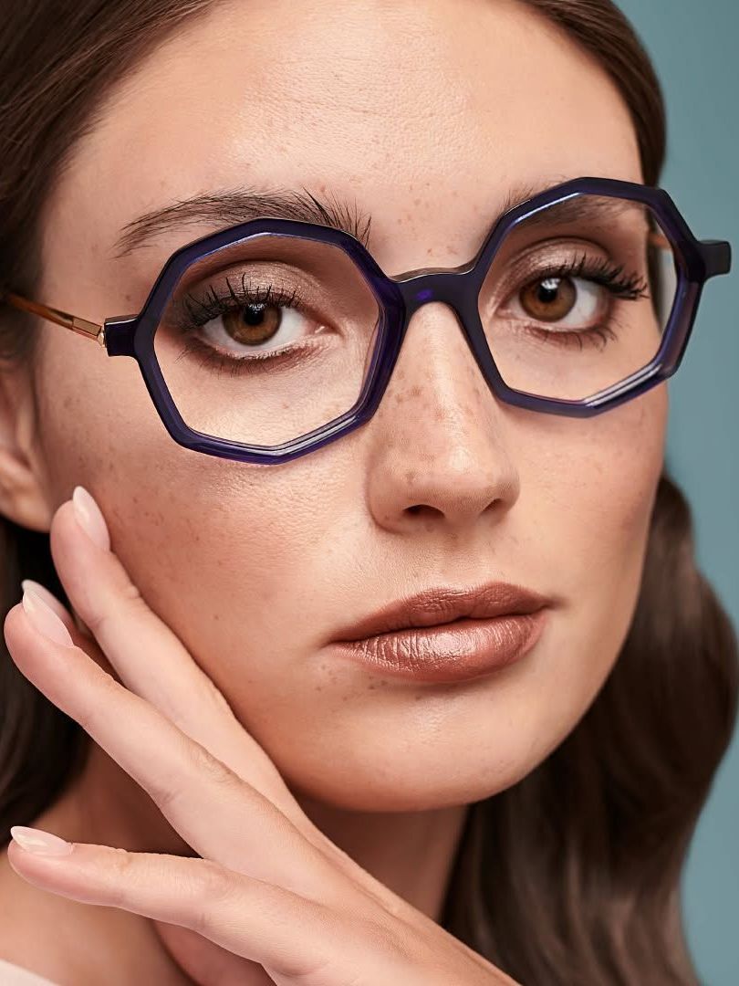 A woman wearing glasses is touching her face with her hand.