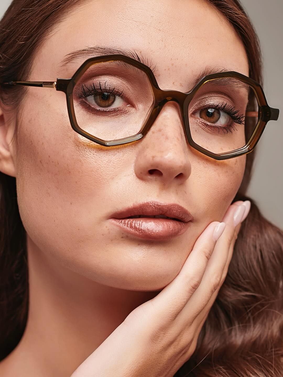 A woman wearing glasses is touching her face with her hand.