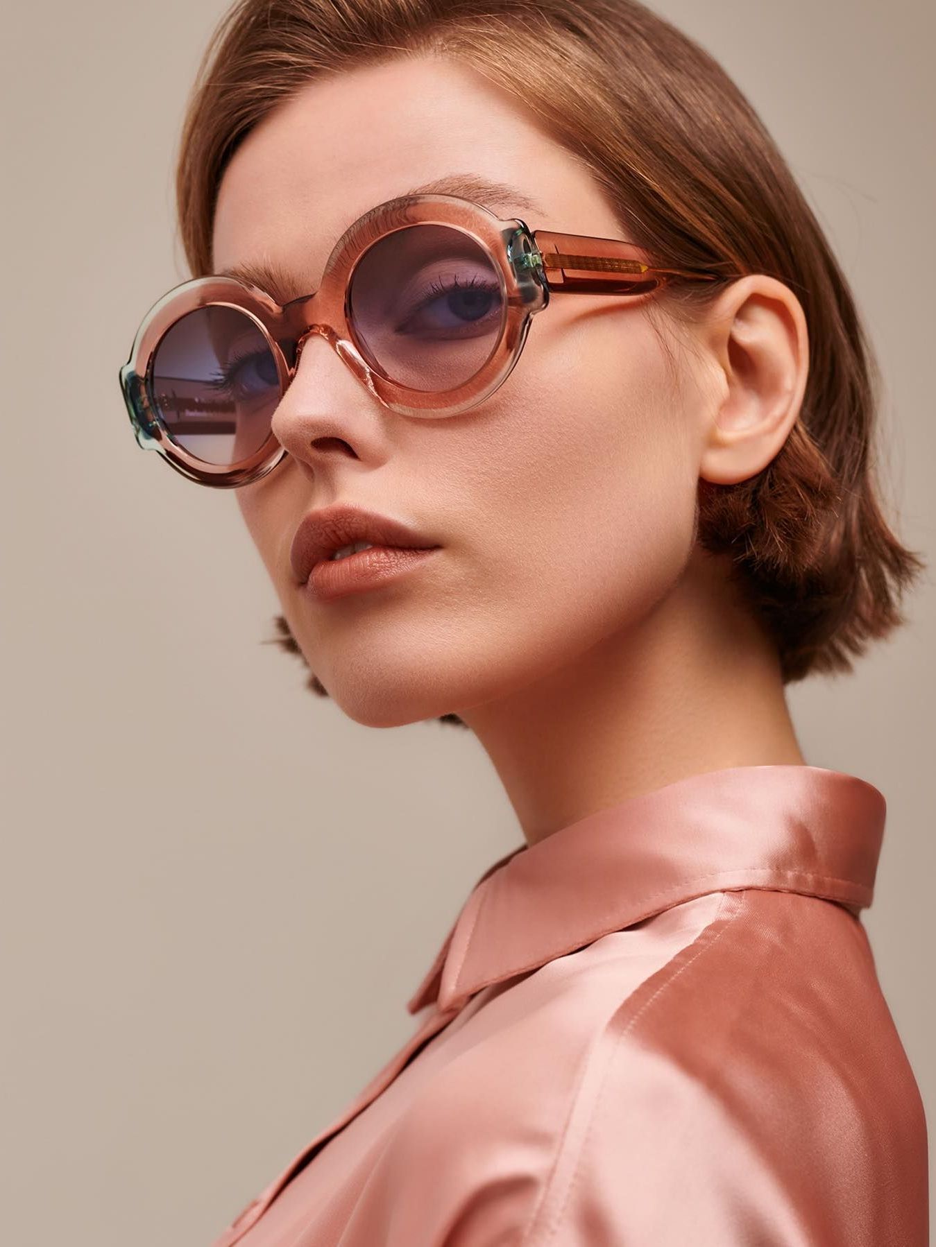 A woman wearing sunglasses and a pink shirt is looking at the camera.