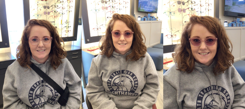 Woman in transitions ruby glasses trying them on in a store. She's wearing a grey hoodie and smiling.