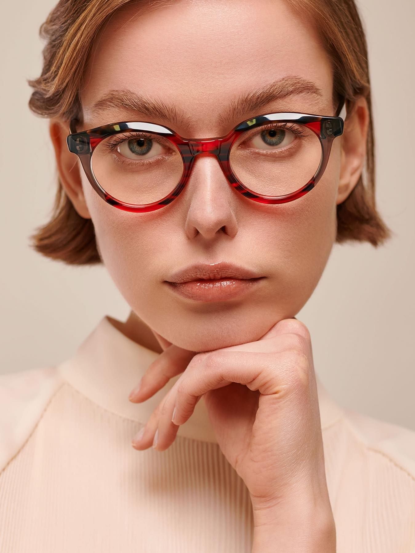 A woman wearing glasses is holding her hand to her chin.