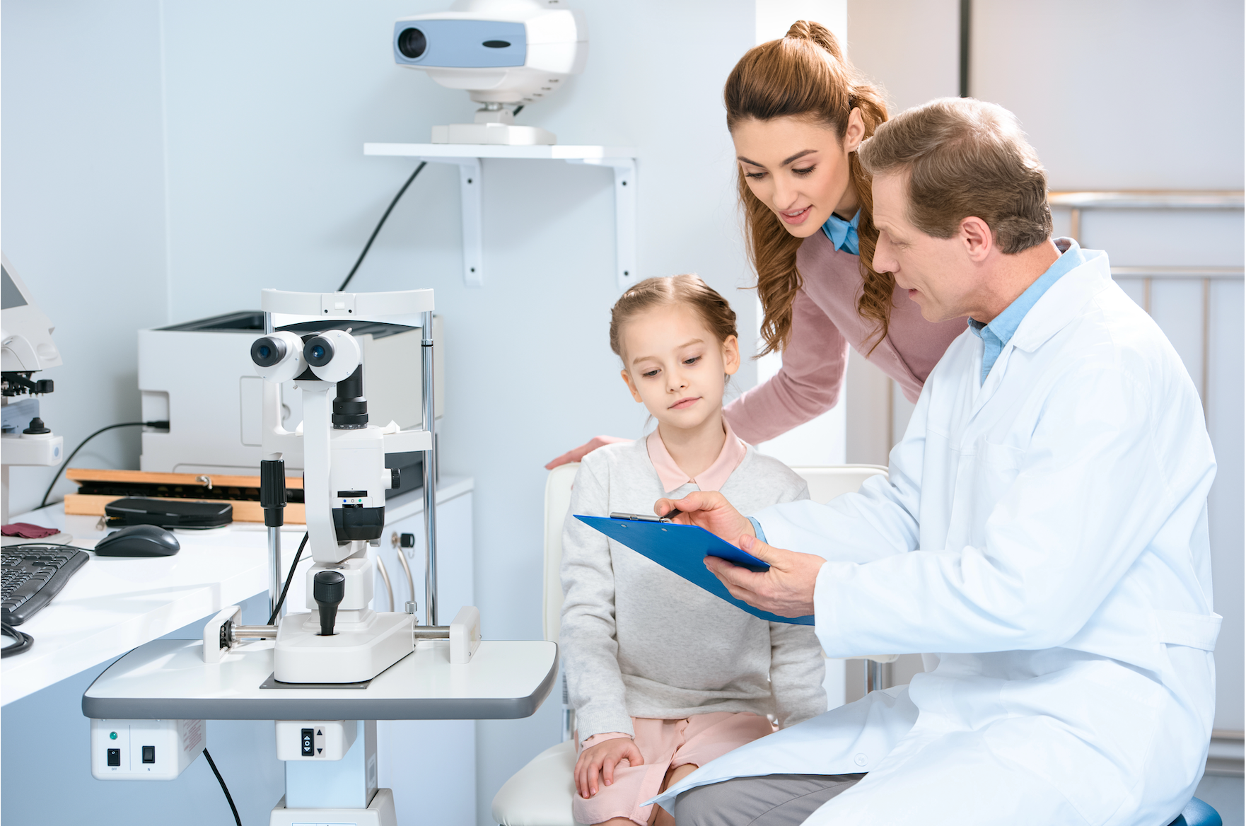 Doctor and family reviewing a clipboard in a bright medical exam room, with lab equipment nearby.