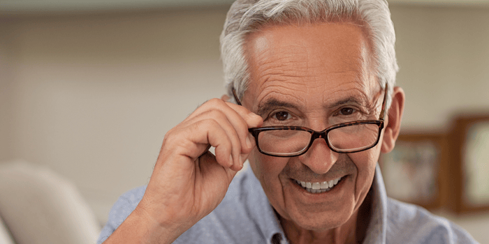 Smiling elderly man with gray hair, wearing glasses, adjusting them with his hand.