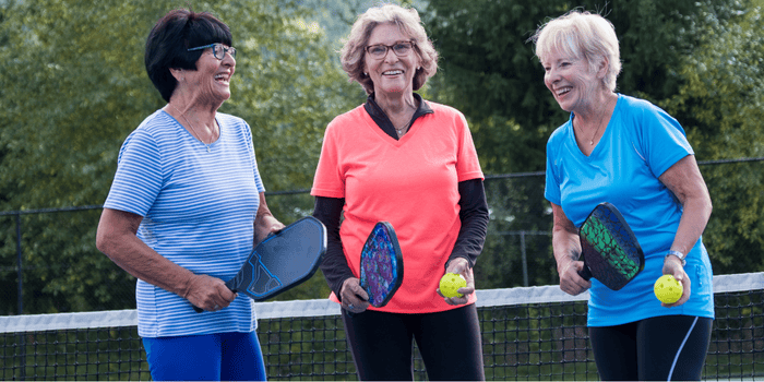 Three older women are playing pickleball on a tennis court.