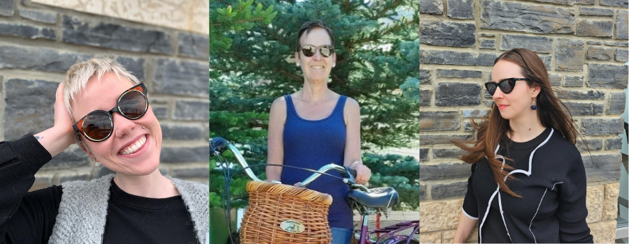 Three women wearing sunglasses smile in front of stone walls and trees. One woman holds a bike.