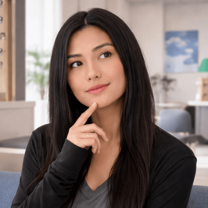 Woman with long dark hair, holding her chin, looking thoughtful, indoors.