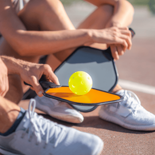 A person is holding a paddle with a tennis ball on it.