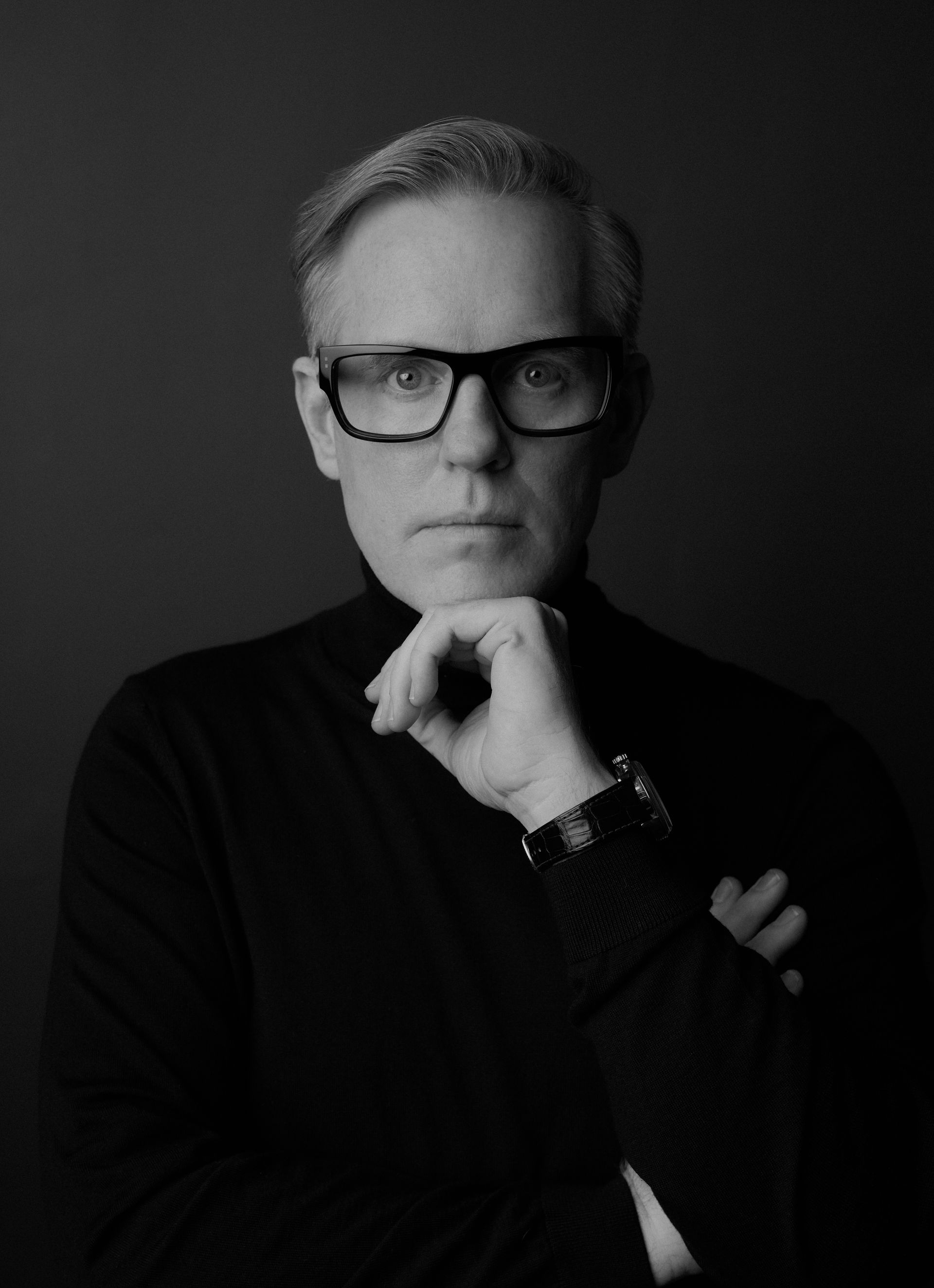 A black and white photo of a man wearing glasses and a black turtleneck.