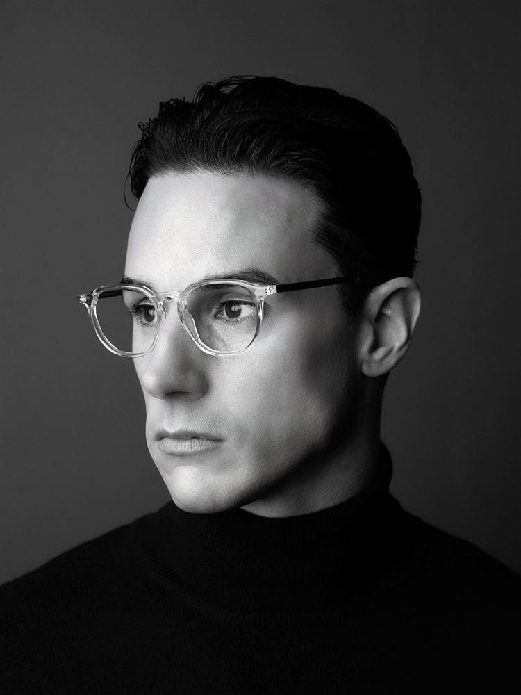 A man wearing glasses and a black turtleneck is in a black and white photo.