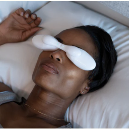 A woman is laying in bed with a white eye mask on her eyes