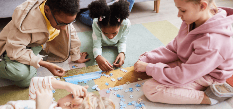 Children assembling a puzzle on the floor, in a brightly colored room, focused.