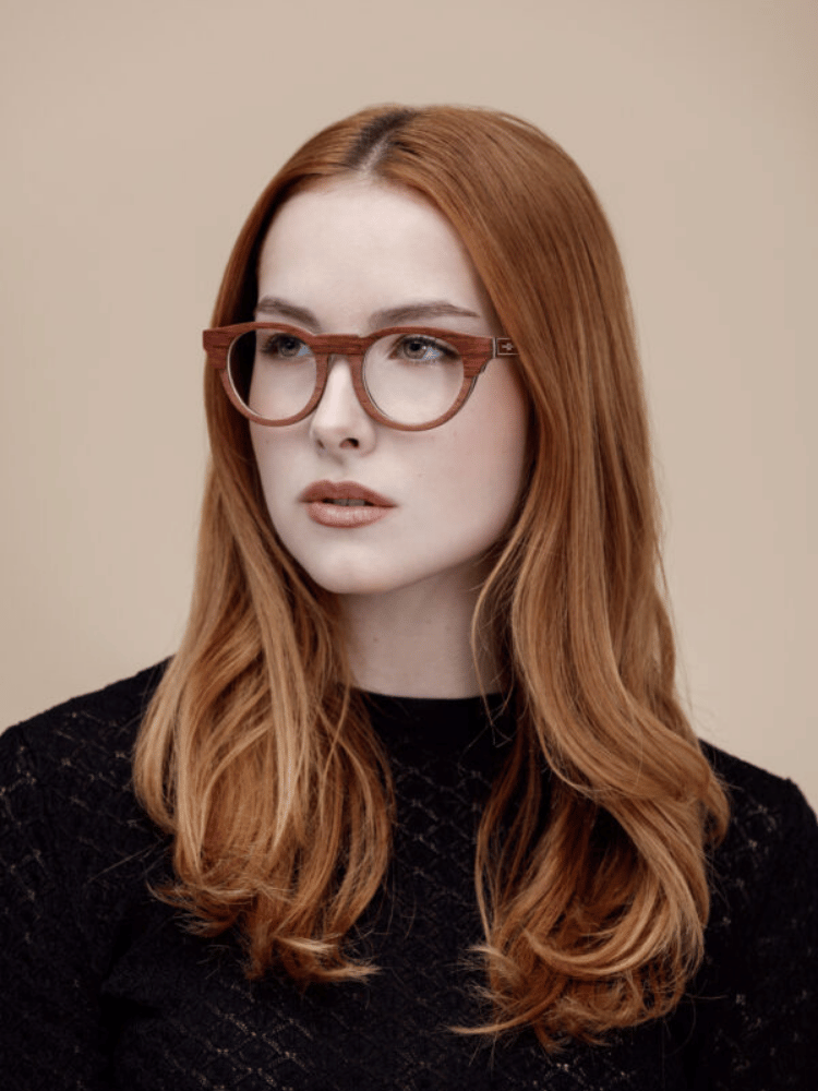 A woman with red hair is wearing glasses and a black sweater.