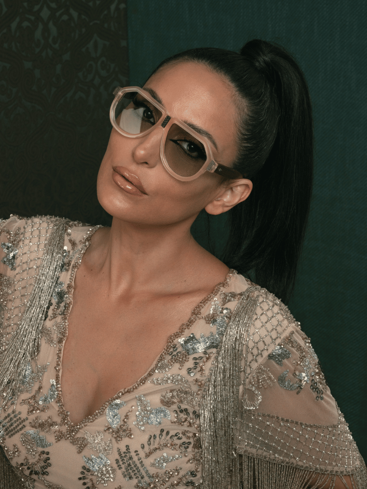 A woman wearing sunglasses and a ponytail is looking at the camera.
