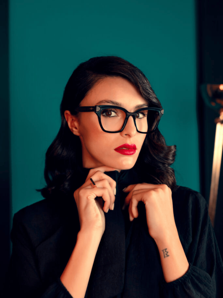 A woman wearing glasses and a black shirt has a tattoo on her wrist