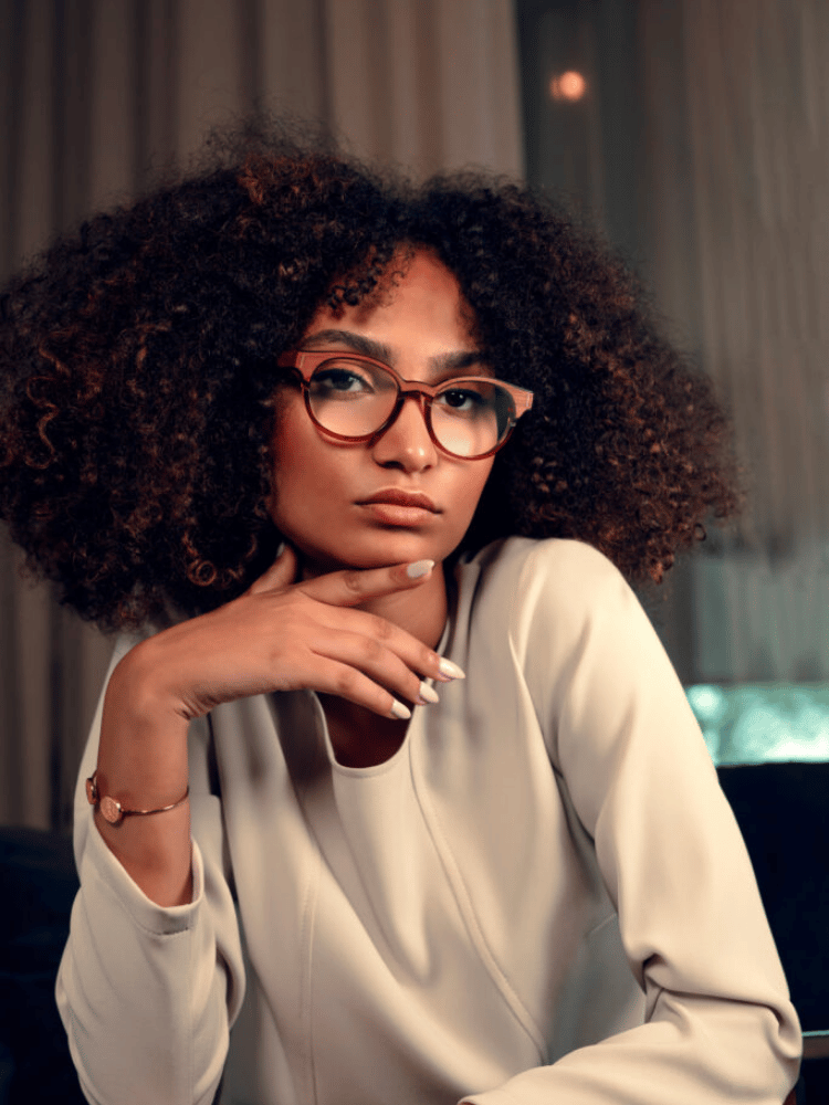 A woman with curly hair is wearing glasses and a white shirt.