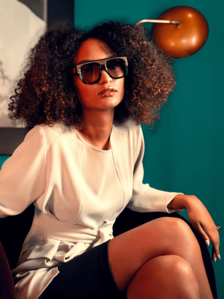 A woman wearing sunglasses and a white dress is sitting on a chair.