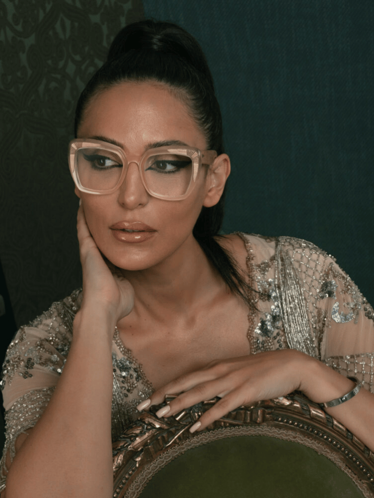 A woman wearing glasses is sitting in a chair with her hand on her face.