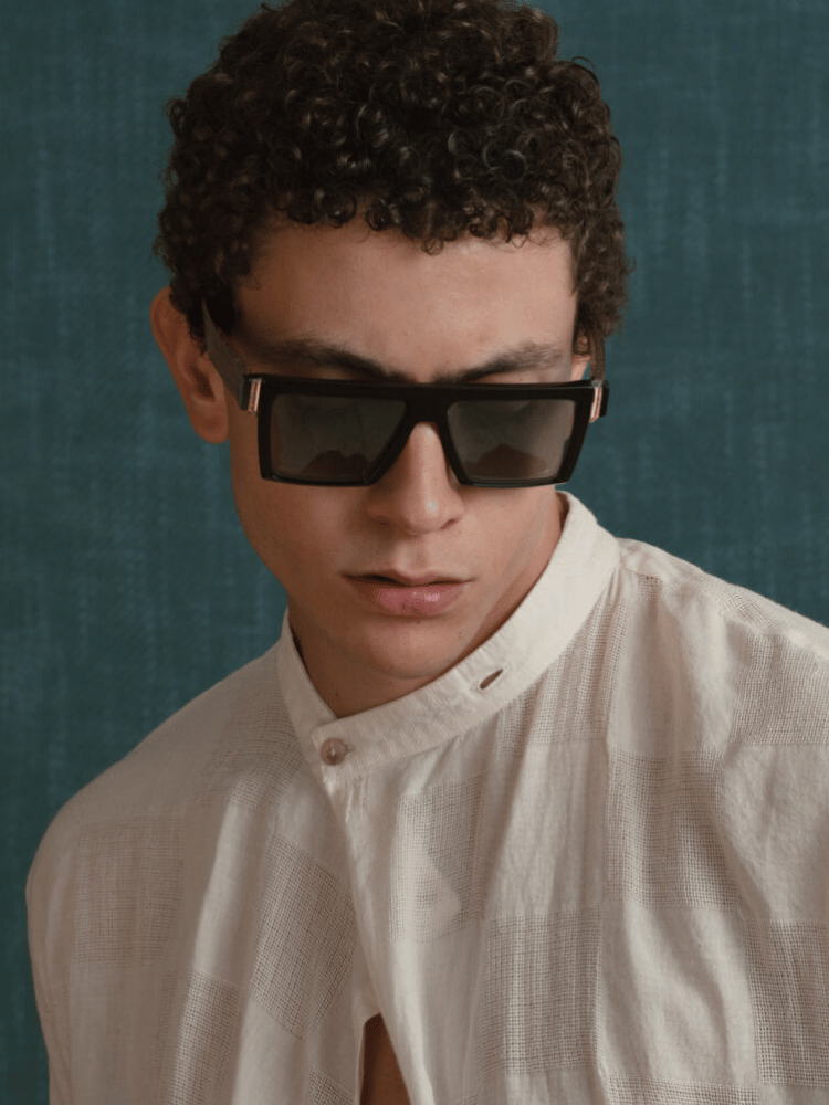 A man wearing sunglasses and a white shirt is looking at the camera.