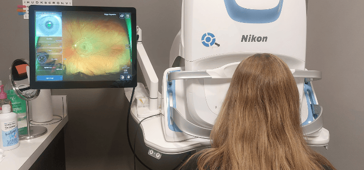 Woman undergoing an eye exam. She sits in front of a Nikon retinal imaging machine, screen shows an eye scan.