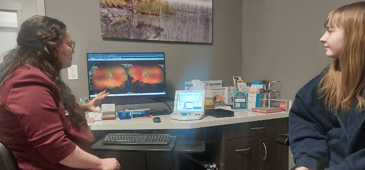 An eye doctor points at a computer screen showing eye scan results to a patient in an office setting.