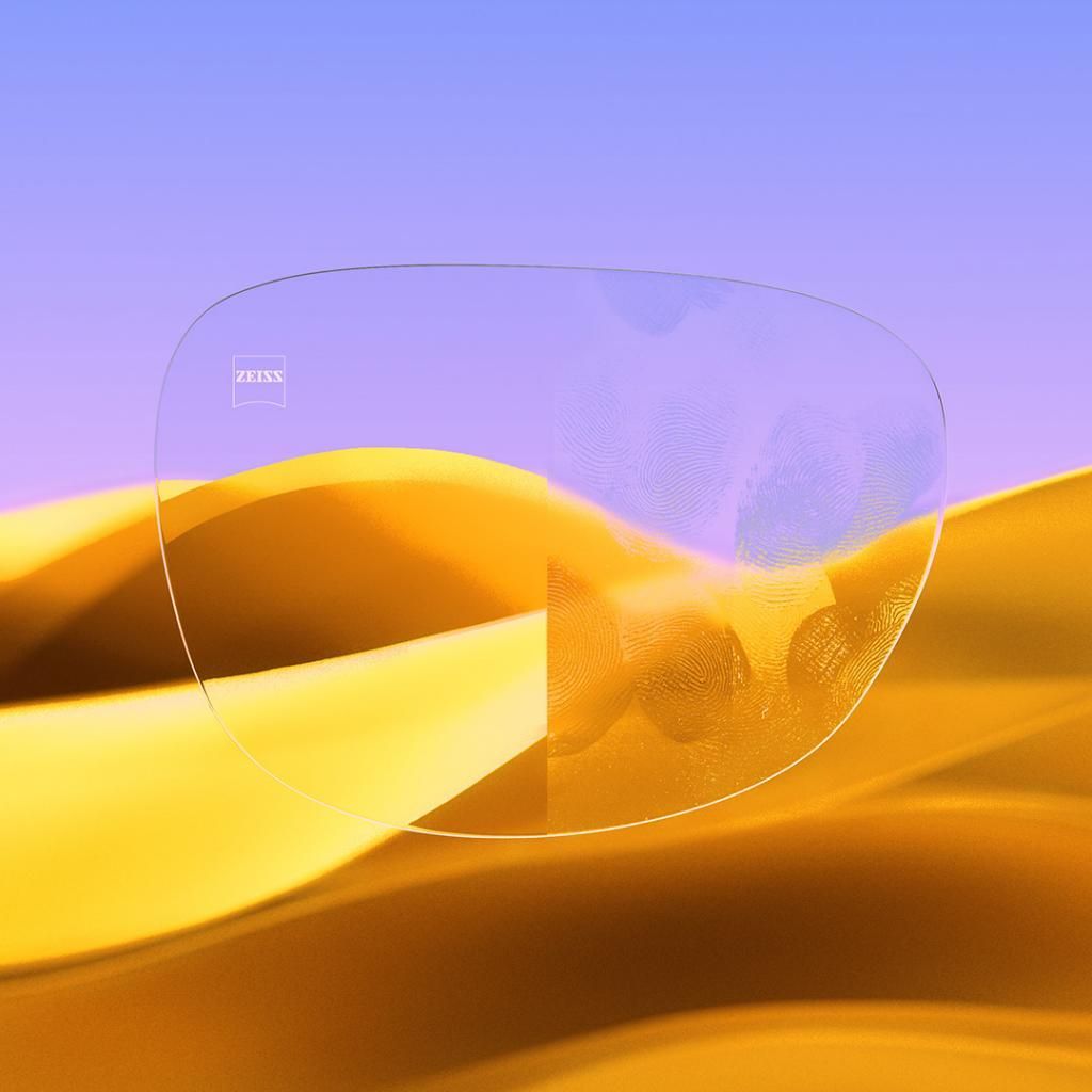 A pair of glasses sitting on top of a sand dune in the desert. One side clean and the other with smudges.