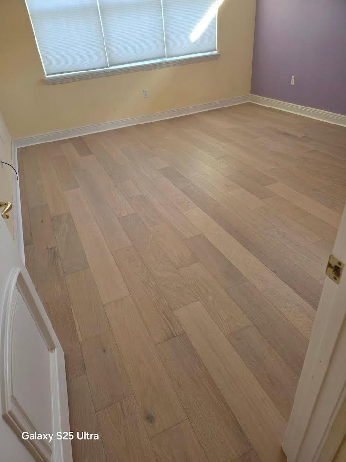 Empty room with light wood floors, beige walls, purple accent wall, and a window with blinds.