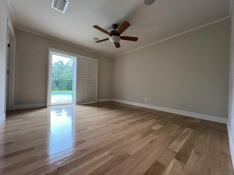Empty beige room with hardwood floors, ceiling fan, and open door to a backyard pool area