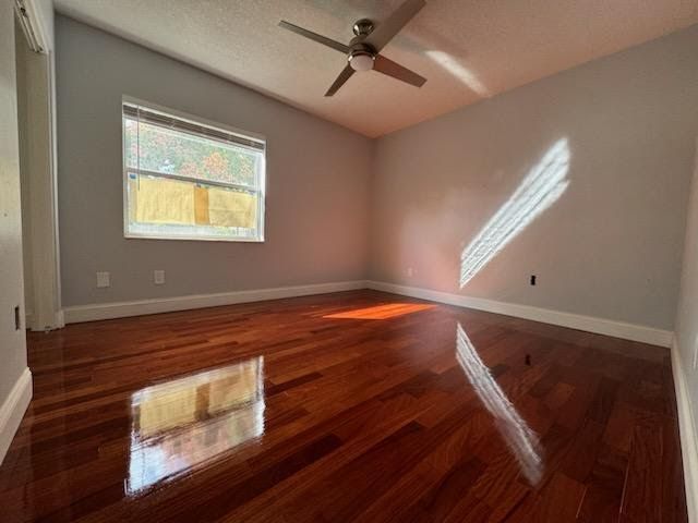 Empty bedroom with glossy hardwood floors, gray walls, a window, and sunlight casting diagonal shadows.