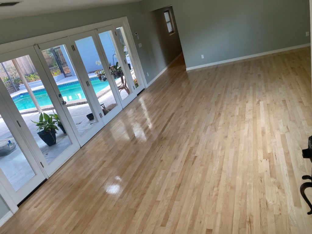 Empty living room with hardwood floors and French doors overlooking a backyard pool.